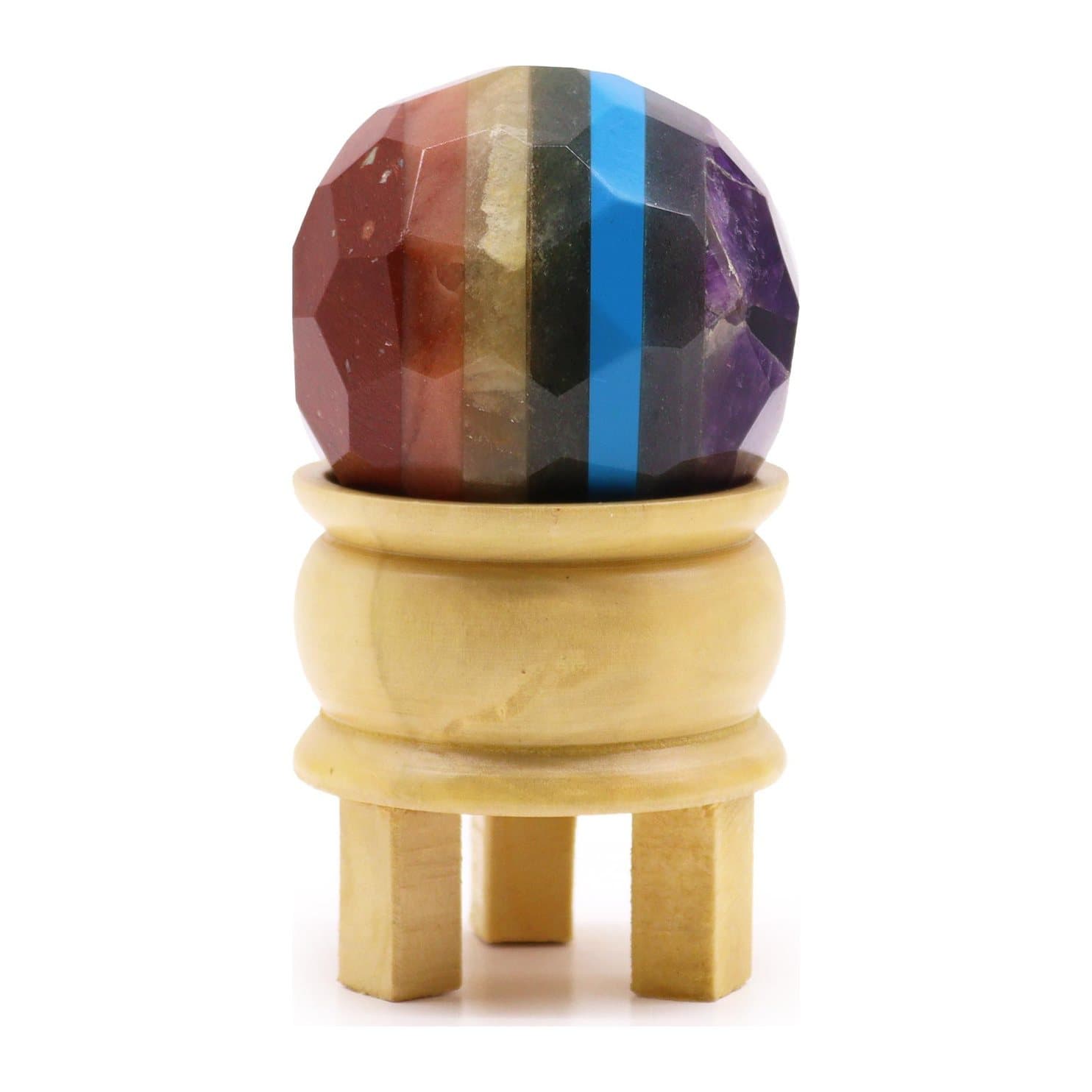 Faceted seven chakra gemstone ball on a light brown wooden stand
