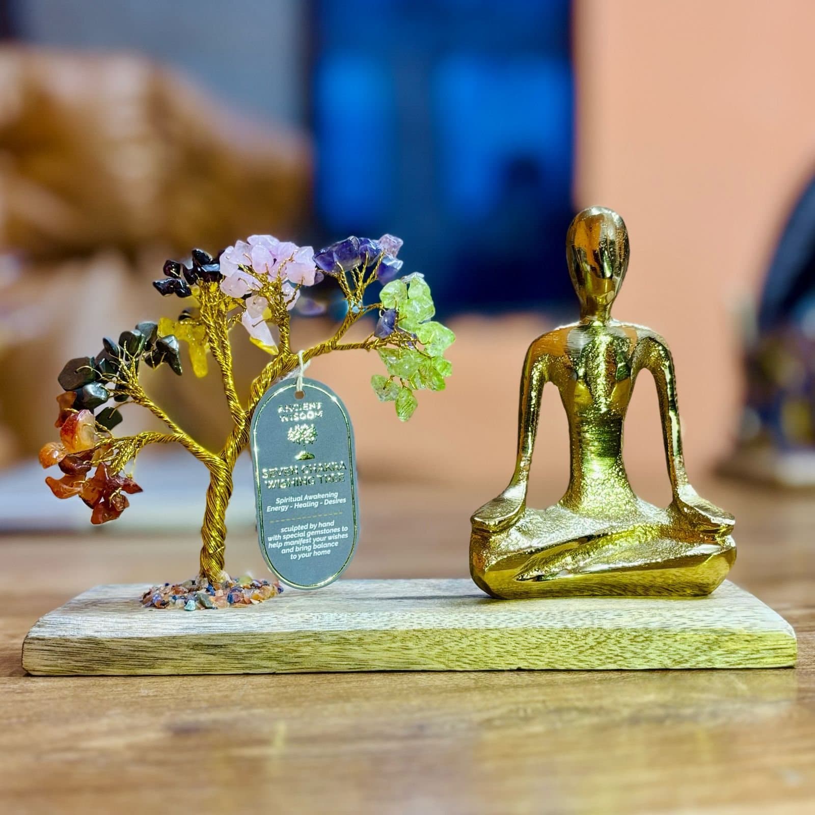 Gold-tone yoga figure beside a tilted gemstone tree on a wooden base