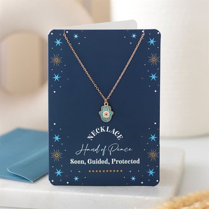 Gold-tone hamsa necklace with turquoise pendant on a dark blue star greeting card