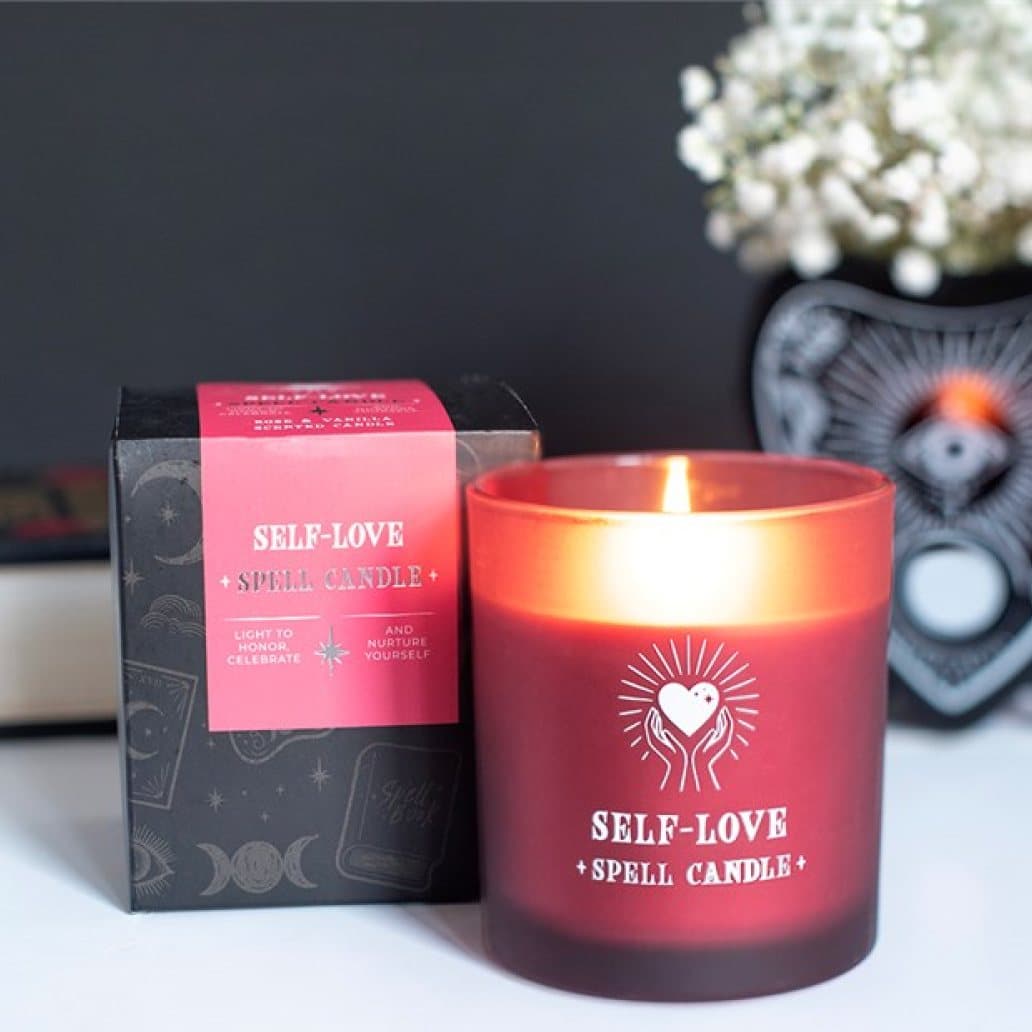 Pink glass jar candle with heart-in-hands artwork beside its matching box