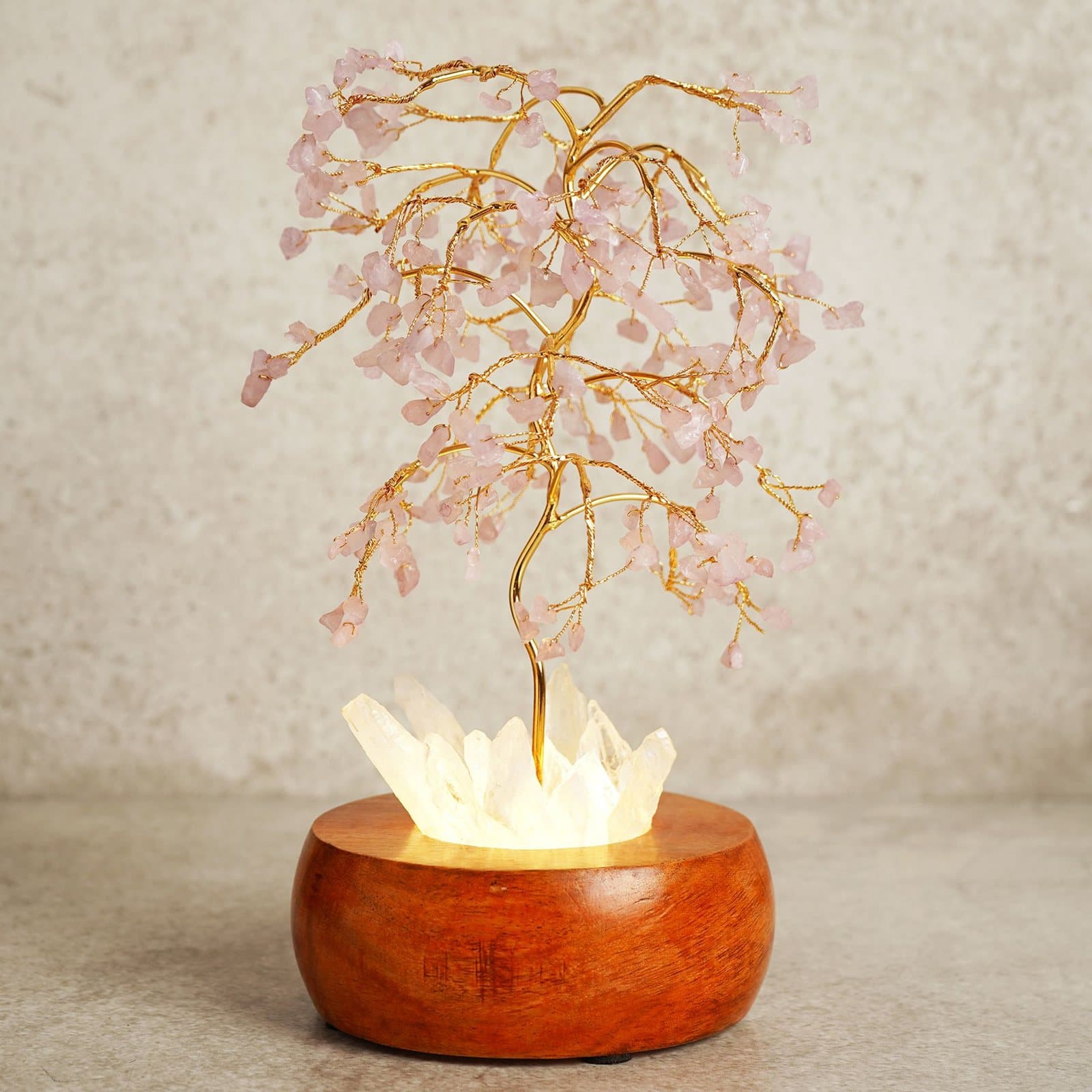 Small tree sculpture of rose coloured crystals on a wooden base glowing from beneath