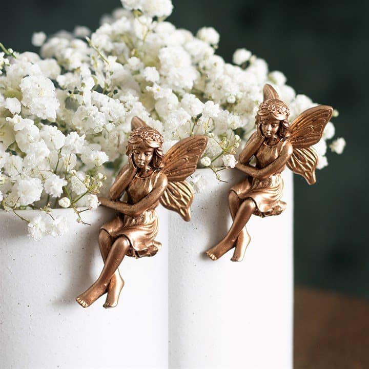 Two antique bronze effect resin fairy figures that perch over a plant pot rim