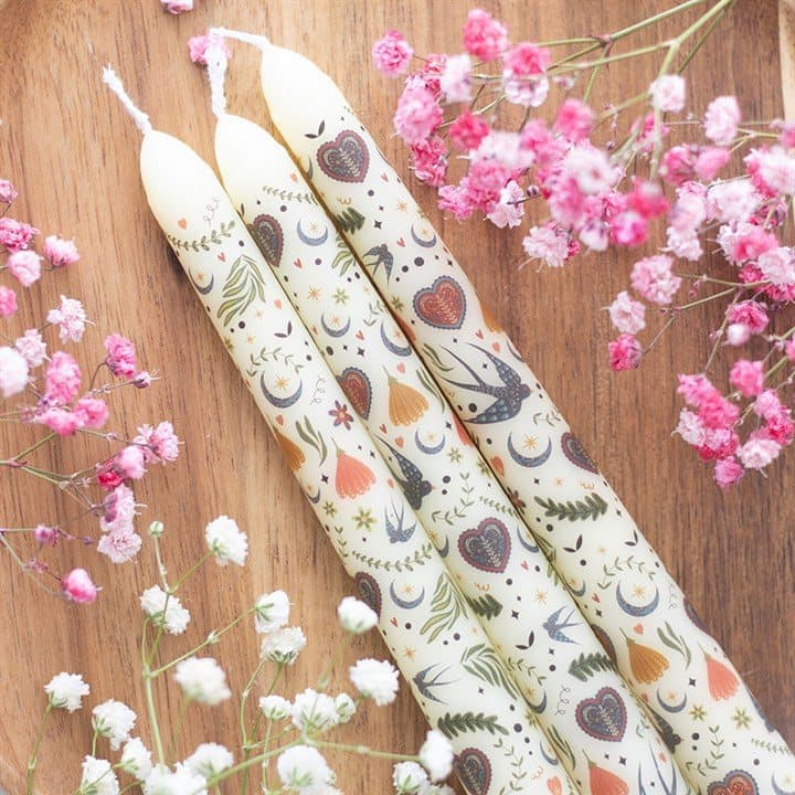 Three cream taper candles with a folk print in a window box