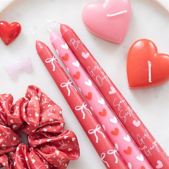 Three taper candles printed with bows and hearts in a window box