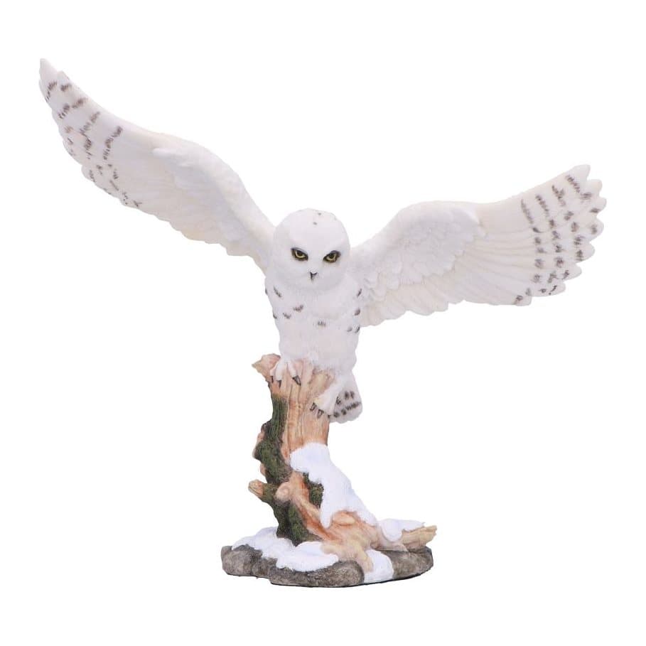 Resin owl with wings spread on a snow-covered log in a winter scene