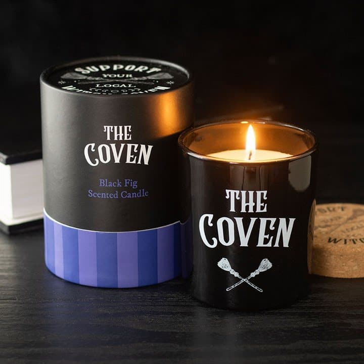 Black glass candle jar with crossed broom design and cork lid beside purple box