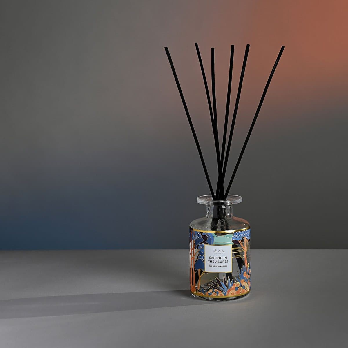 Glass reed diffuser bottle with wooden reed sticks beside a coastal design box